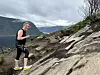 En kvinne går på en steinete fjellsti med vann og fjell i bakgrunnen.