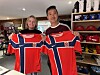 To personer står i en butikk og holder opp røde Norge-fotballdrakter.