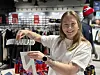 Smilende kvinne holder opp et Haaland-trykk i en sportsbutikk med røde og hvite norske fotballdrakter.