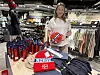 Kvinne står i en sportsbutikk og holder en rød og blå fotballskjorte ved et bord med Norgesutstyr.