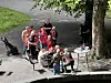 En gruppe mennesker i røde klær står og sitter samlet ved en brygge ved siden av vannet.