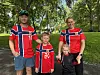 To voksne og to barn står i en park iført røde drakter med norsk flaggmønster.