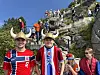 En stor folkemengde i røde klær står og sitter i en bratt steintrapp med fjell og blå himmel i bakgrunnen.