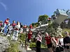 En stor folkemengde i røde klær står og sitter langs en bratt steintrapp i solskinn.
