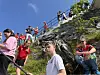 Flere personer i røde og hvite klær står og går i en bratt steintrapp ved fjellsiden under åpen himmel.