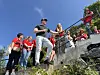 Folk i røde klær står og sitter i en bratt steintrapp utendørs under klar himmel.