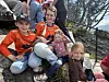 Flere personer sitter tett sammen på en trapp, mange i røde klær, med et by- og fjellandskap i bakgrunnen.