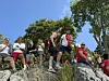 En gruppe mennesker sitter på svaberg under trær i solfylt vær.