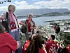En gruppe mennesker i røde drakter står og sitter ved et utsiktspunkt med utsikt over sjø, by og fjell.