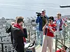 Flere personer i røde klær står ved et rekkverk med utsikt over en by og fjorden.