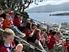En gruppe mennesker i røde klær sitter på svaberg og benker med utsikt over Ålesund og sjøen.