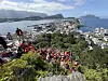 Stor folkemengde i røde drakter sitter og står i en bratt trappeskråning med utsikt over Ålesund og fjorden.