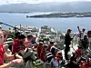En stor gruppe mennesker i røde klær sitter og står på en utsiktshøyde med byen og fjorden i bakgrunnen.