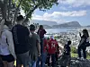 Gruppe mennesker står på en sti med utsikt over Ålesund, sjøen og fjellene.