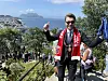 En mann med solbriller og rød skjerf står foran en stor folkemengde på en trapp med fjord og fjell i bakgrunnen.