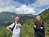 To menn står ute i naturen foran et grønt fjellandskap og en skyet himmel.