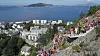 Stor folkemengde i rødt og hvitt står langs en fjellsti med utsikt over byen og fjorden.
