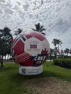 Stor dekorativ fotball med norsk flagg og teksten «Miami Beach welcomes team Norway» på gressplass med palmer.