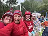 Fire kvinner sitter tett sammen og smiler på en utendørs festival med publikum i bakgrunnen.