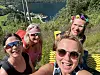 Fire kvinner tar en selfie på et utsiktspunkt med fjord og båter i bakgrunnen.