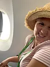 Smilende kvinne i stråhatt sitter ved flyvinduet.