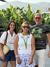 Tre personer står foran bananplanter og fjell i sollys.