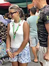 Kvinne i hvit topp og mønstret shorts står i en folkemengde på et utendørsmarked.