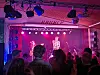 Publikum står foran en belyst scene med to musikere og røyklys under en konsert.