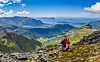 To personer sitter på en steinete fjellrygg med utsikt over dal, fjord og hav.