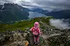 Et barn i rosa klær står på en steinete fjellrygg med utsikt mot fjord og fjell.