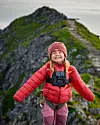 Smilende barn i rødt yttertøy og lue står på en smal fjellrygg med kamera festet på brystet.