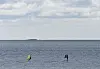 To kitesurfere på vannet med en lav øy i horisonten og skyer over.