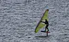 En vindsurfer står på brettet og seiler over vannet med et fargerikt seil.