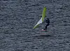 En vindsurfer står på brettet sitt på bølgete vann med et grønt og hvitt seil.