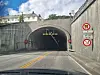 En bil kjører mot en mørk tunnelinnkjøring med skilt på begge sider. Tunnel. Valderøytunnelen. Ellingsøytunnelen.