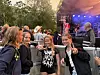 Fire ungdommer står foran en utendørsscene med lys og musikere i bakgrunnen.