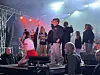 Flere personer står på en scene med scenelys, røyk og publikum i forgrunnen.