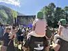 Folkemengde sitter og står på en gressbakke foran en utendørsscene med lys og fjell i bakgrunnen.