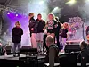 Et band står på en opplyst scene med røyk, lysrigg og publikum foran.