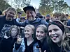 Flere personer står tett samlet utendørs foran et telt og smiler mot kamera.