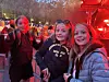 Tre ungdommer står tett sammen og smiler foran rødt lys utendørs i skumringen.