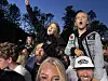 En gruppe mennesker står tett sammen utendørs og jubler med armene i været i kveldslys.