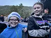 To barn står foran et utendørs publikum med fjell og trær i bakgrunnen.