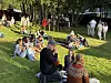 Flere mennesker sitter og ligger på en grønn gressbakke i en park på en solskinnsdag.