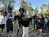 En gruppe barn og ungdommer står ute på gresset, noen løftet opp på andres skuldre, omgitt av trær.