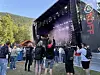 Folk står samlet foran en stor scene med scenelys og røyk under åpen himmel.