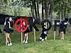 Fire personer står og sitter ved store bokstaver ute på gresset i en park med trær i bakgrunnen.