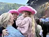 To jenter med rosa cowboyhatter klemmer hverandre i en folkemengde foran en stor scene.