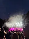 Folkemengde foran en utendørsscene med sterke lys, røyk og mørk kveldshimmel.