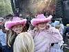 To barn i rosa cowboyhatter smiler foran en festivalscene med publikum og røyk i bakgrunnen.